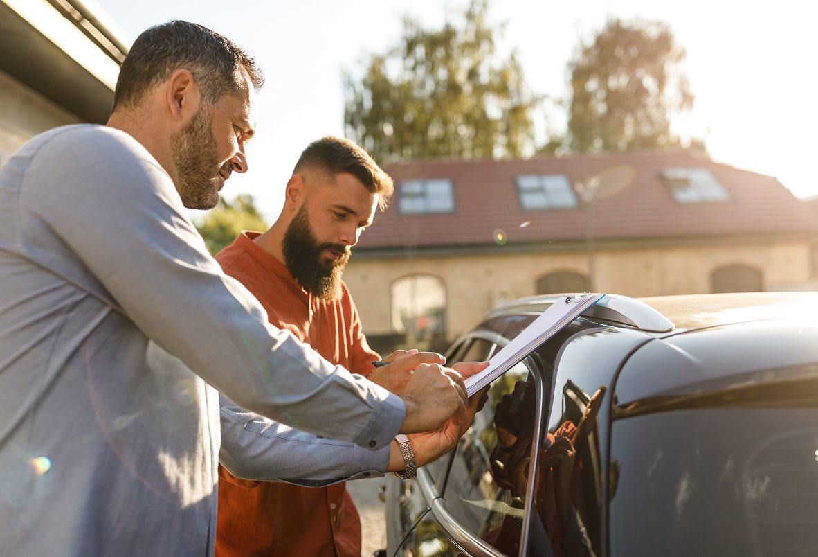 Two men reviewing documents on a car.