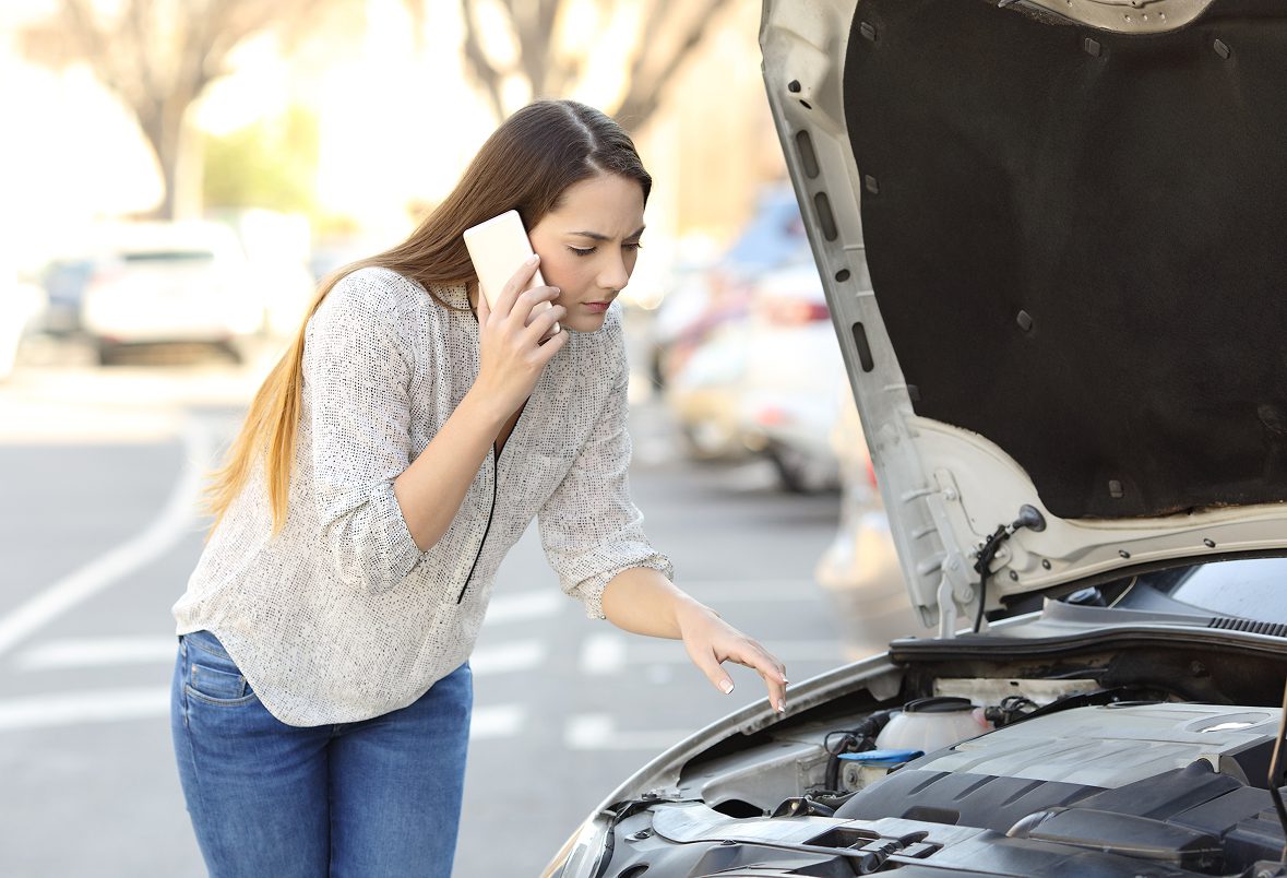 Woman on phone beside broken down car.