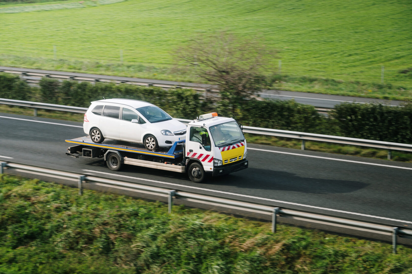 Tow truck transporting a white car on highway.