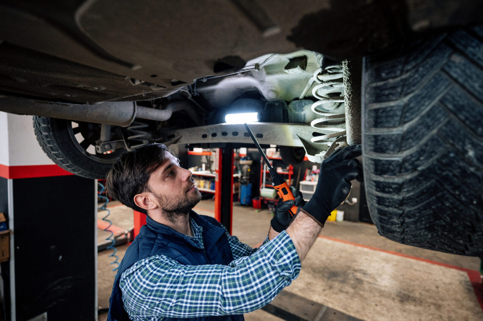 Mechanic inspecting car's underside in garage.