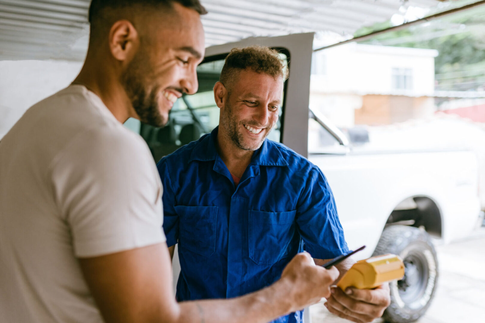 Two men smiling and using a device.