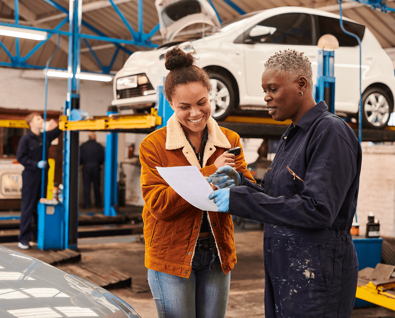 Two women discussing paperwork in car workshop.